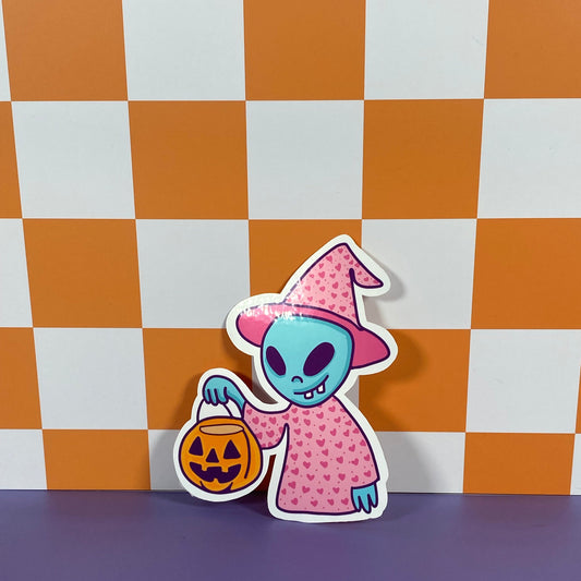 Halloween-themed alien sticker with a pink dress and witch hat on a checkered background