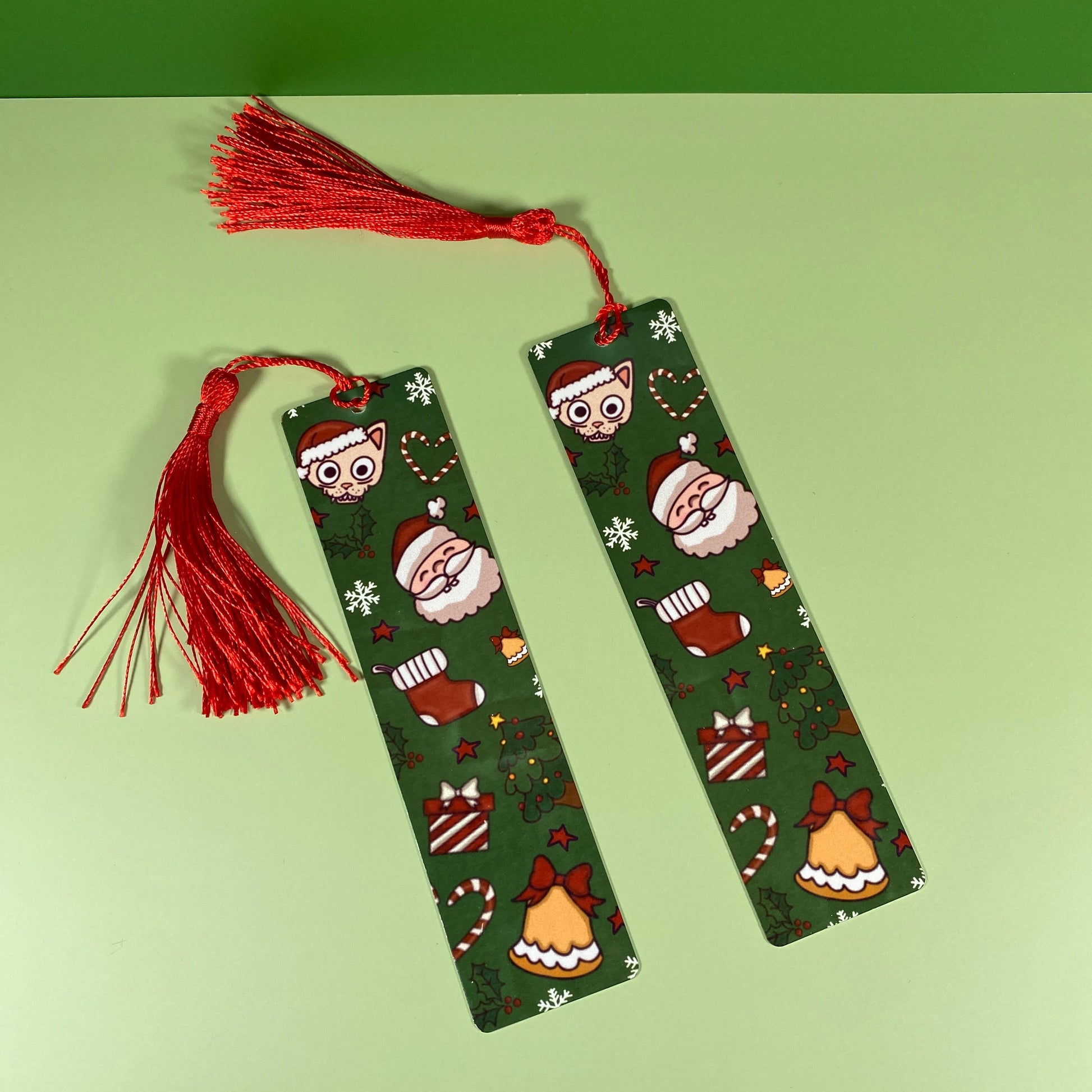 Two green bookmarks with festive designs and red tassels on a green background