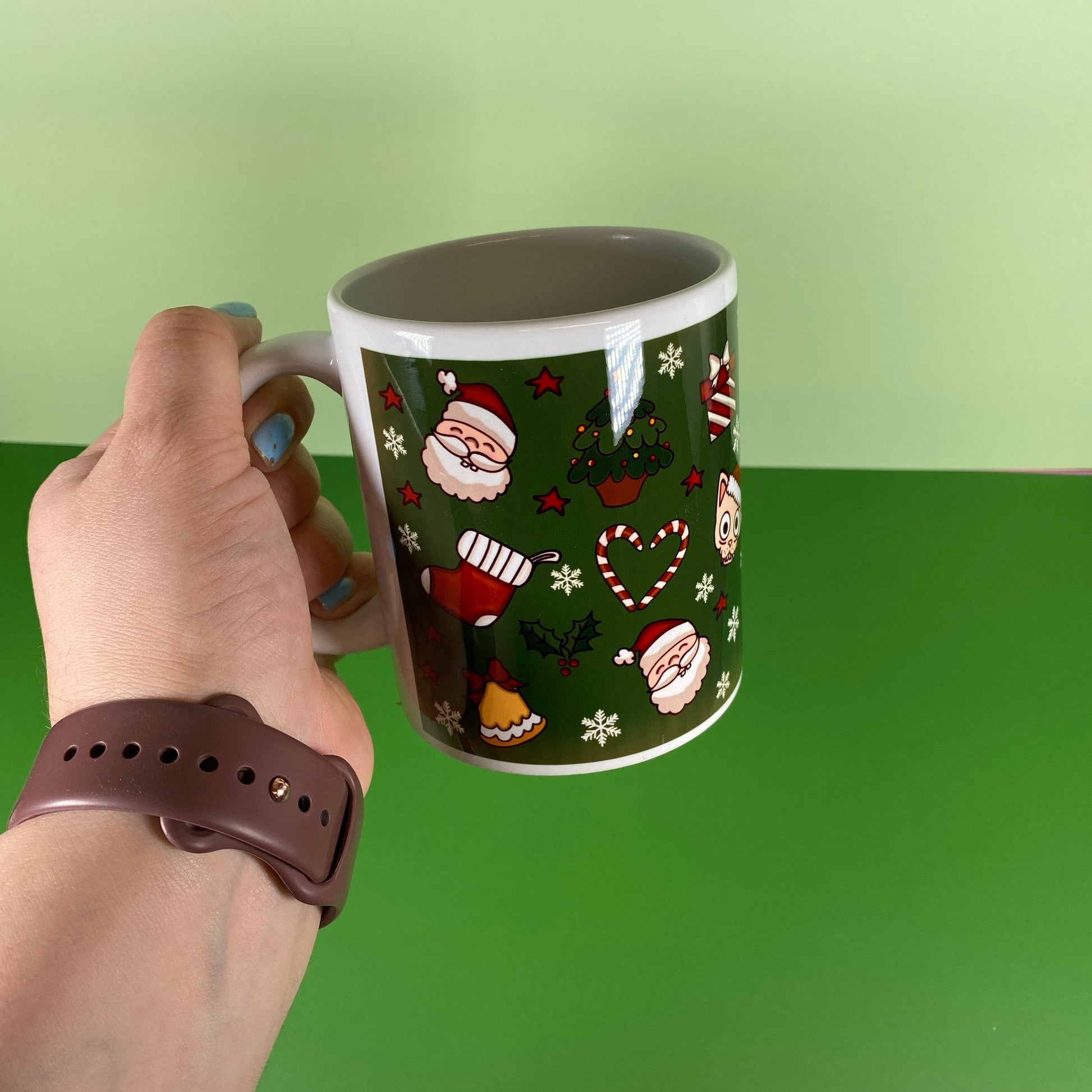 Hand holding a mug with Christmas-themed design against a green background