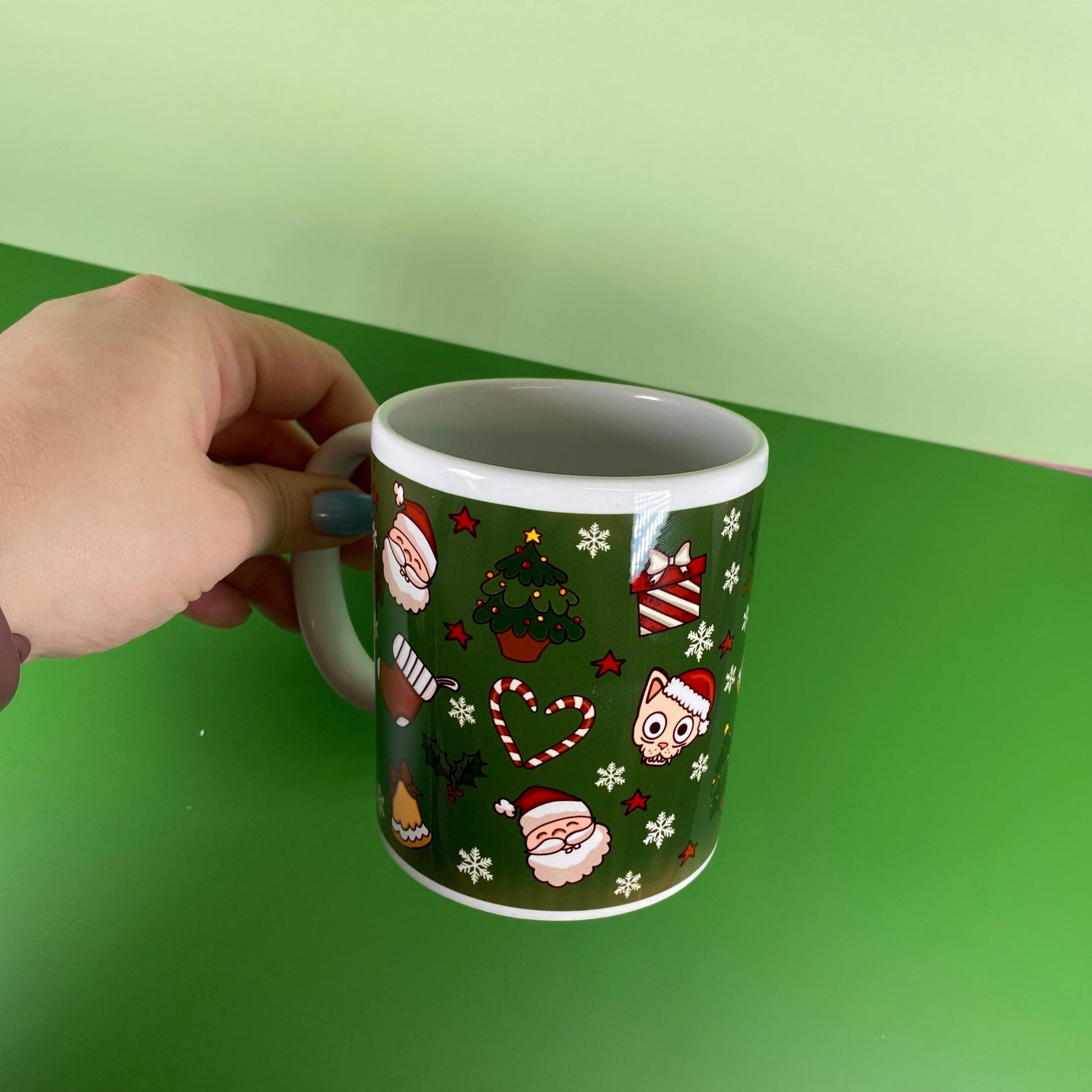 Hand holding a mug with Christmas-themed design against a green background